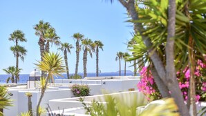Un hotel costero de paredes blancas, palmeras y vista al mar.