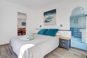 Une chambre à coucher avec un lit, deux oreillers, une table de chevet, un tableau et une vue sur une salle de bain carrelée.