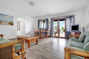 Une pièce avec un plancher en bois, un canapé, une table à manger avec des chaises, un téléviseur et une lampe.