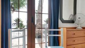 Una habitación con un aparador de madera, una silla, un ventilador y vistas a palmeras a través de una puerta de cristal.