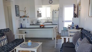 A modern living room with a sofa, a dining table, and a kitchen area with a sink and countertop. - Ithaki 2 Bedroom Penthouse (Λατσί/ Πόλη Χρυσοχούς)