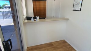 A small, clean room with a wooden floor, a white wall, a window with blinds, a framed map, and a counter with a bottle of hand sanitizer. - Sun City Motel (Bundaberg North)