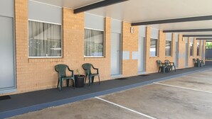 A row of single-room hotel units with large windows, a brick facade, and a covered outdoor area with chairs and a trash bin. - Sun City Motel (Bundaberg North)
