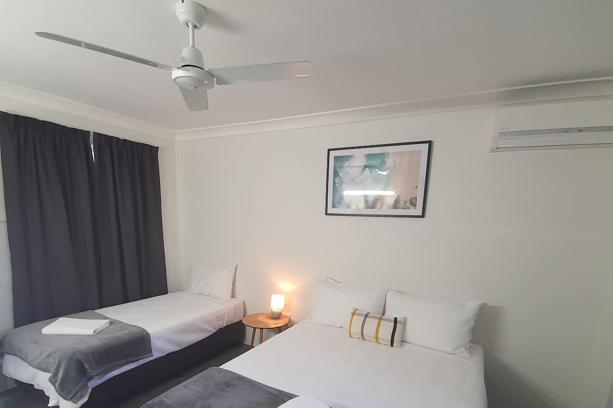 A hotel room with two beds, a ceiling fan, a bedside lamp, and a framed picture on the wall.