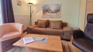 En stue med sofa, lænestol, sofabord, gulvlampe og et billede på væggen.