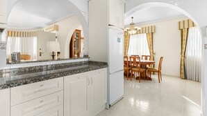 Une cuisine avec des meubles blancs, un plan de travail en granit, un réfrigérateur et un coin repas comprenant une table et des chaises.