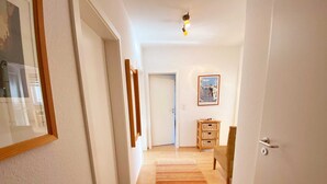 Un corridoio con pavimento in legno, un tappeto a righe, una porta, un piccolo armadietto in legno e un quadro appeso al muro.