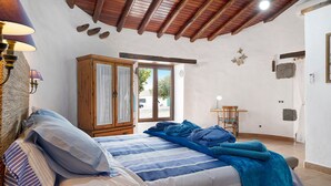 Une chambre à coucher avec un lit, une armoire en bois et une vue sur l’extérieur, visible à travers une porte.