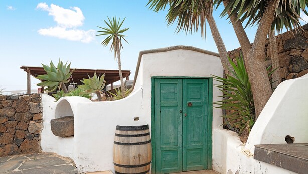 A white building with a green door, a stone wall, and a large barrel. - Holiday Home with Mountain Views, Balcony and Wi-Fi (Los Valles)
