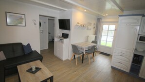 Un espacio habitable compacto con sofá, una pequeña mesa de comedor, zona de cocina con microondas y televisor montado en la pared.