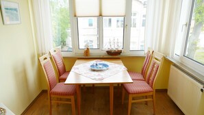 Ein Essbereich mit Tisch und vier Stühlen, ein Fenster mit Blick auf Gebäude und eine Heizung an der Wand.