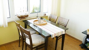 Uma área de refeições com uma mesa de madeira, quatro cadeiras, toalha de mesa listrada, modelo de navio e uma janela com cortinas.