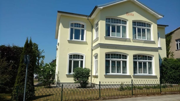 Um edifício de dois andares com fachada amarelo claro, várias janelas e uma placa com o nome 