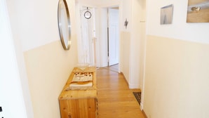 Um corredor com piso de madeira, um banco de madeira, um espelho e uma porta no final.