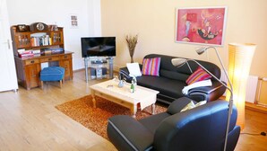 Uma sala de estar com sofá, mesa de centro, televisão, estante de livros e um quadro na parede.