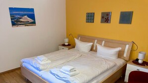 Quarto de hotel com uma cama grande, duas mesas de cabeceira, uma cadeira vermelha e um quadro na parede.