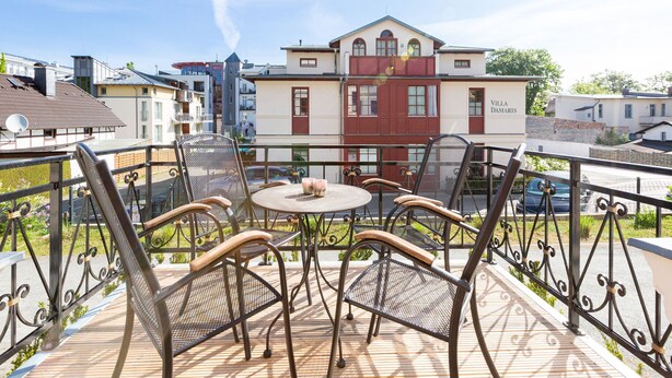 Ein Balkon mit Sitzgelegenheit im Freien, Blick auf ein Gebäude mit der Aufschrift 'Villa Damaris' und einem klaren Himmel.