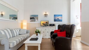 Ein Wohnzimmer mit einer Couch, einem Sessel, einem Couchtisch und einem Fernseher.