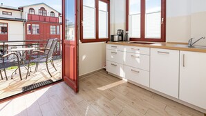 Eine moderne Küche mit großen Fenstern, einem Essbereich mit Metallstühlen und Blick auf benachbarte Gebäude.