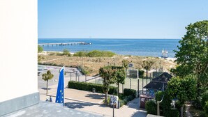 Vistes costaneres amb un moll que s'endinsa a la mar, una zona enclouda amb vegetació i un edifici amb una bandera blava.