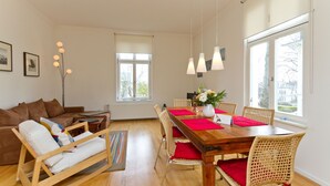 A modern living room with a wooden dining table, wicker chairs, and a sofa.