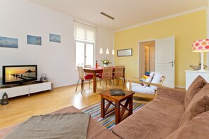 Un salon comprenant un canapé, un téléviseur, une table à manger avec des chaises, une lampe et des œuvres d’art accrochées aux murs.
