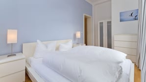 A bedroom with a large bed, white bedding, two bedside tables with lamps, and a door leading to another room.