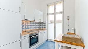 A modern kitchen with white cabinets, a blue tiled backsplash, a wooden countertop, and a large window.
