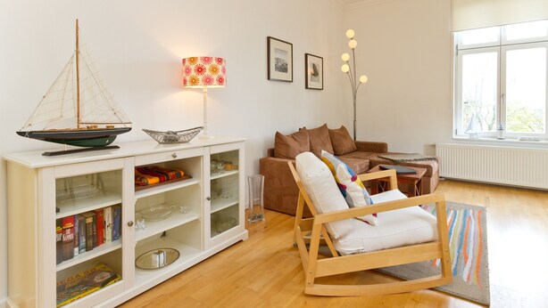 A living room with a wooden rocking chair, a white cabinet with glass doors, a small sailboat model, and a lamp with a floral lampshade.