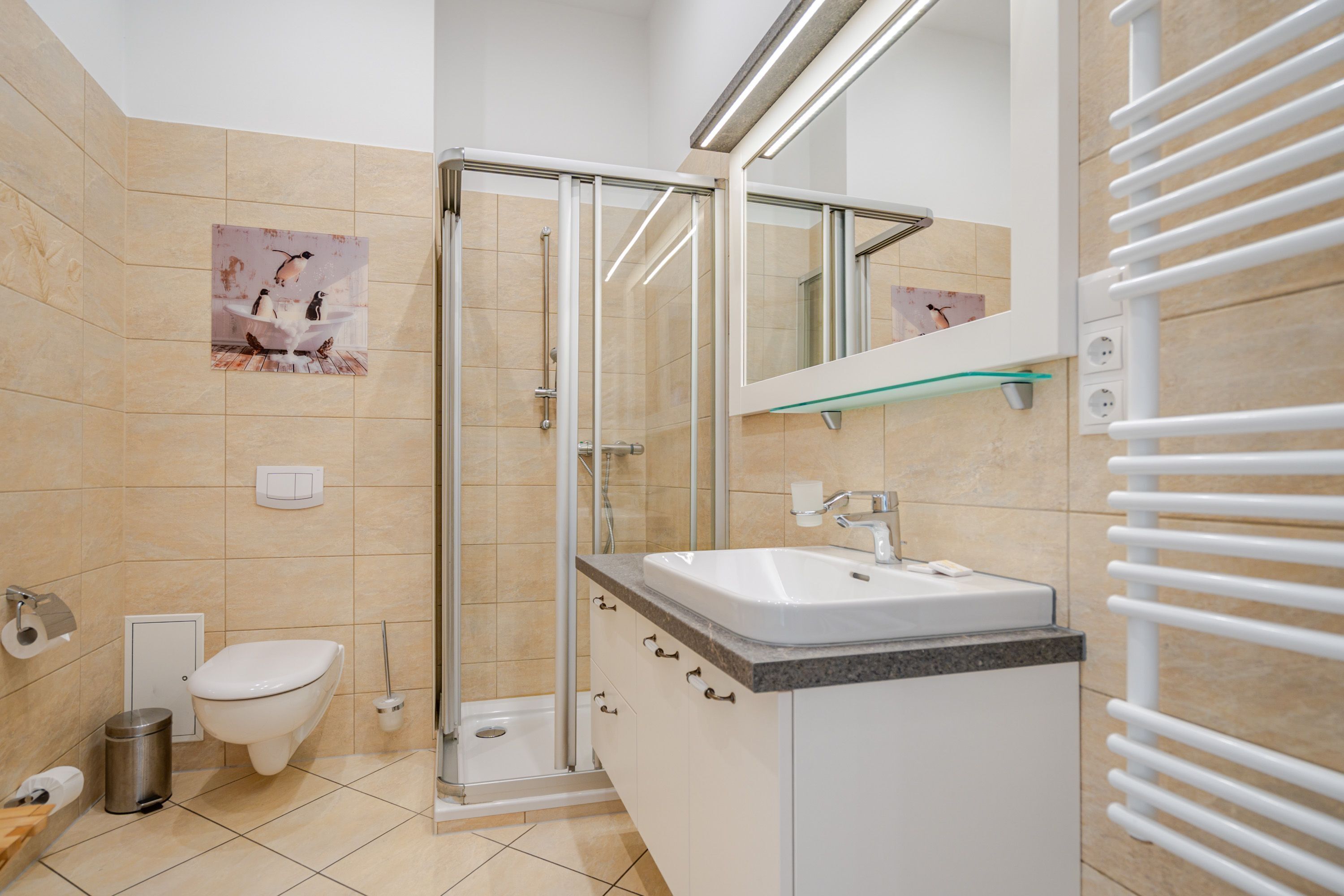 Een moderne badkamer met een douchecabine van glas, een wit toilet en een wastafel met een marmeren aanrecht.