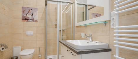 A modern bathroom with a glass shower enclosure, a white toilet, and a sink with a marble countertop.