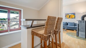 Een moderne keuken met een bar, twee rieten stoelen, een eettafel en uitzicht op de stad door een raam.
