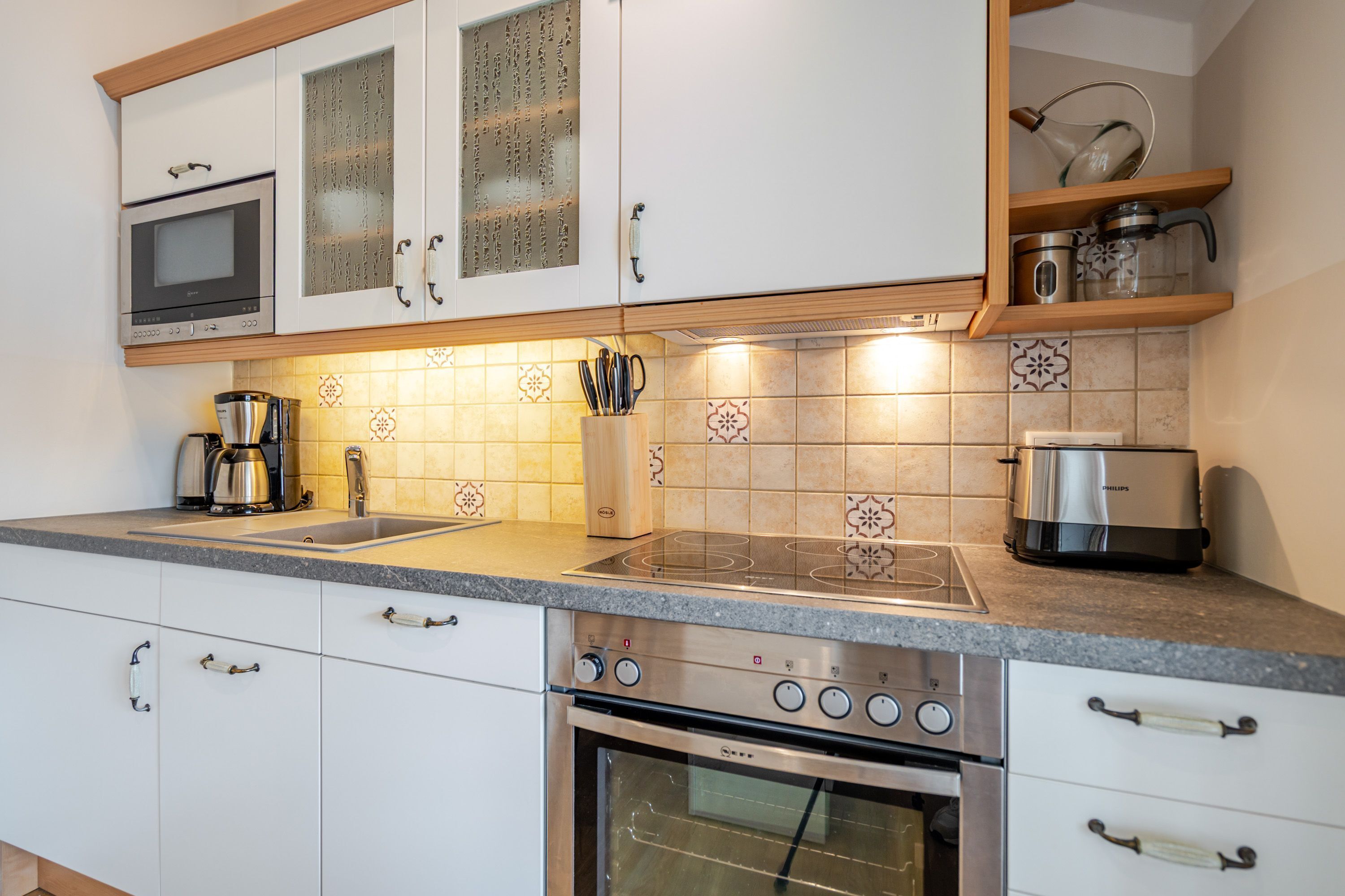 A modern kitchen with white cabinets, a built-in oven, a coffee maker, and a toaster.