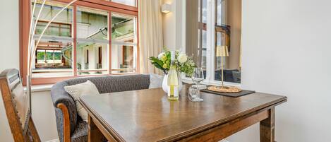 A dining area with a wooden table, chairs, a vase with flowers, and a window with curtains.