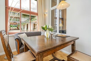 A dining area with a wooden table, chairs, a vase with flowers, and a window with curtains.