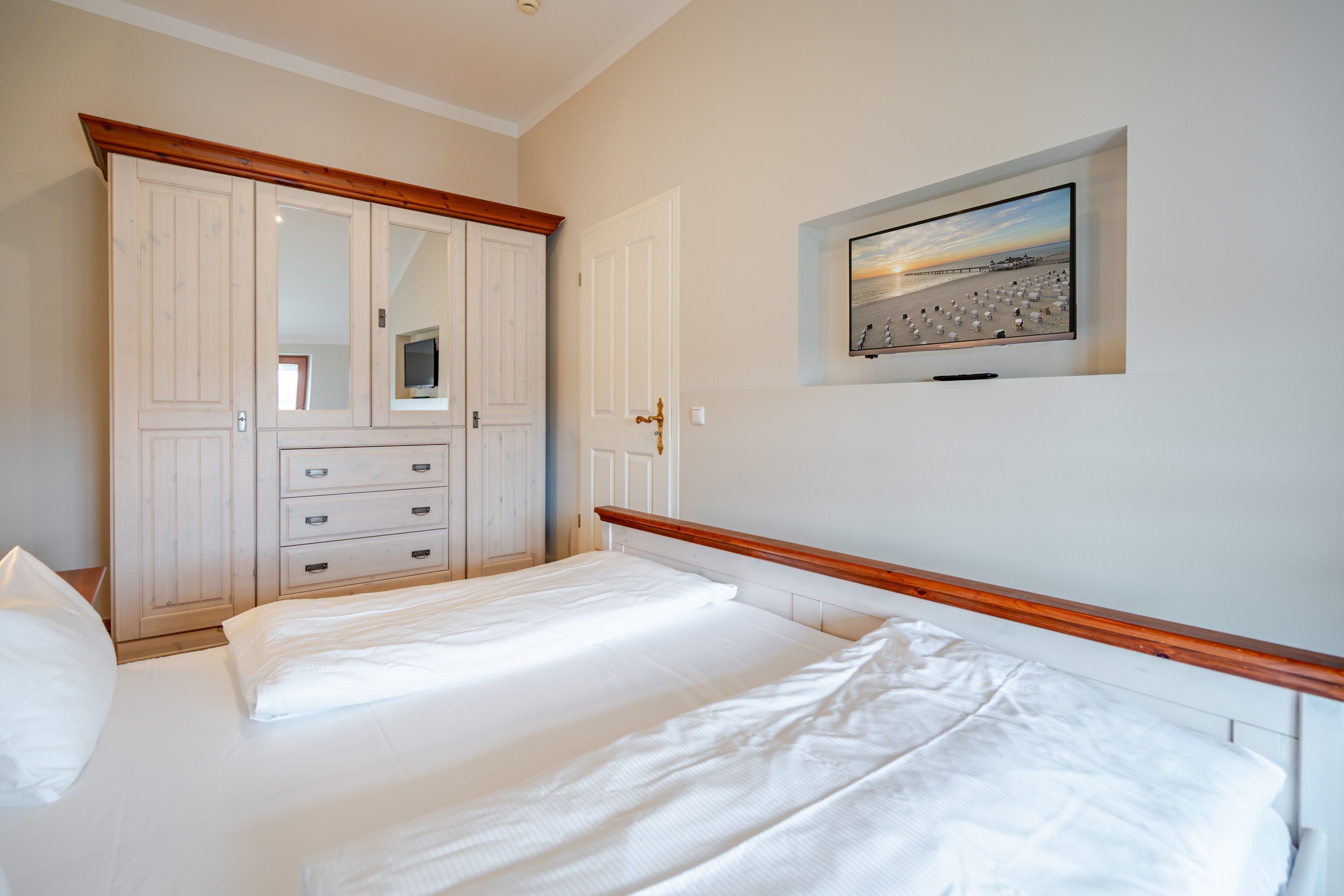 Quarto com cama, guarda-roupa, televisão e um quadro com uma cena de praia.
