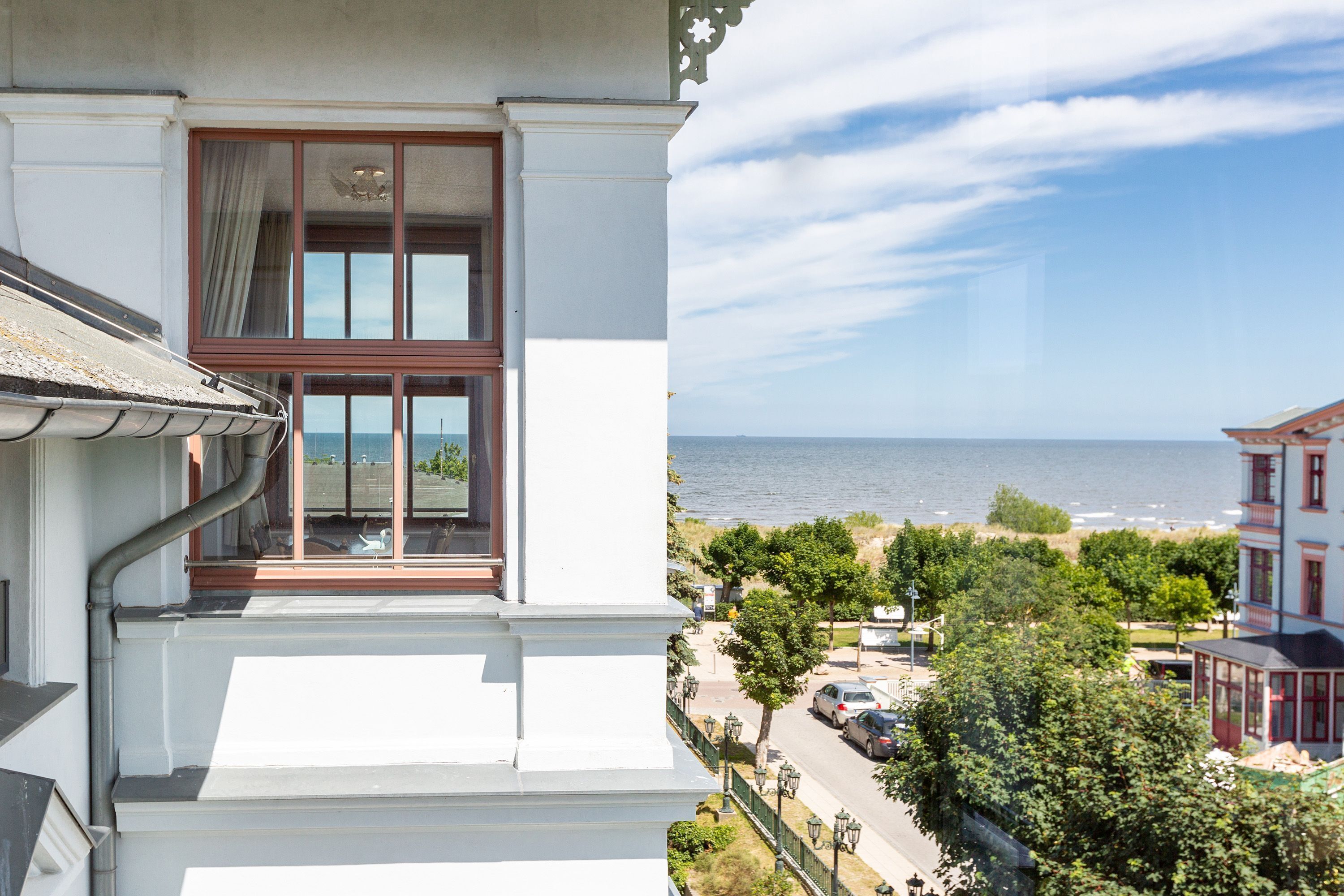 A balcony with a view of the sea and a street with parked cars.