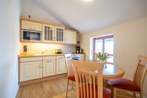 A kitchen with wooden cabinets, a microwave, and a coffee maker. There is a dining table with chairs and a vase of flowers. - The Author's House, App. 15 Lasker student (Heringsdorf)