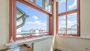 Une pièce dotée d’une grande fenêtre donnant sur un paysage urbain, d’un radiateur et d’une petite table sur laquelle est posé un modèle de bateau.