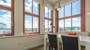 Un espace repas comprenant une table et des chaises, de grandes fenêtres donnant sur l’extérieur et un banc agrémenté d’un coussin.