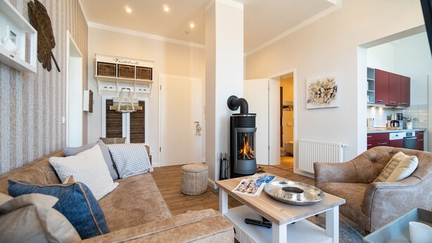 Ein gemütliches Wohnzimmer mit Kamin, einer Couch, einem Couchtisch und einer Küche im Hintergrund.