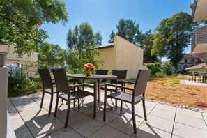 Une terrasse extĂ©rieure avec une table ronde et six chaises, entourĂ©e dâun jardin et dâarbres.