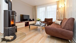 A modern living room with a wood-burning stove, a sofa, a coffee table, and a TV. - Residenzen am Kulm, Villa Dorian 18 (Heringsdorf)