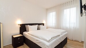 A modern bedroom with a large bed, a nightstand, and a wall-mounted TV. - Residenzen am Kulm, Villa Dorian 18 (Heringsdorf)