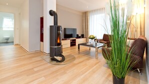 A modern living room with a wood-burning stove, a flat-screen TV, a sofa, and a coffee table. - Residenzen am Kulm, Villa Dorian 18 (Heringsdorf)