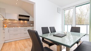 A modern kitchen with white cabinets, a glass dining table, and black chairs. - Residenzen am Kulm, Villa Dorian 18 (Heringsdorf)