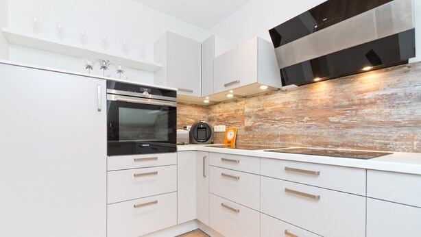 A modern kitchen with white cabinetry, a built-in oven, and a wooden backsplash. - Residenzen am Kulm, Villa Dorian 18 (Heringsdorf)