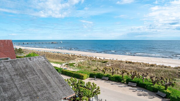 Een kustgezicht met strand, een pier en een parkeerplaats met bankjes.