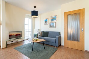 Ein modernes Wohnzimmer mit grauem Sofa, einem Glastisch, einem Flachbildfernseher und einer Holztür.