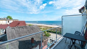 Een balkon met een tafel en stoelen met uitzicht op een strand en de oceaan.